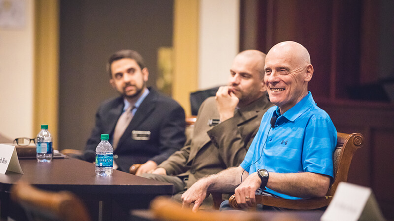 Dr. Hugh Ross, Regent University Lecturer sitting at a table and smiling with Dr. Corné Bekker, Dean, School of Divinity, sitting to his left.