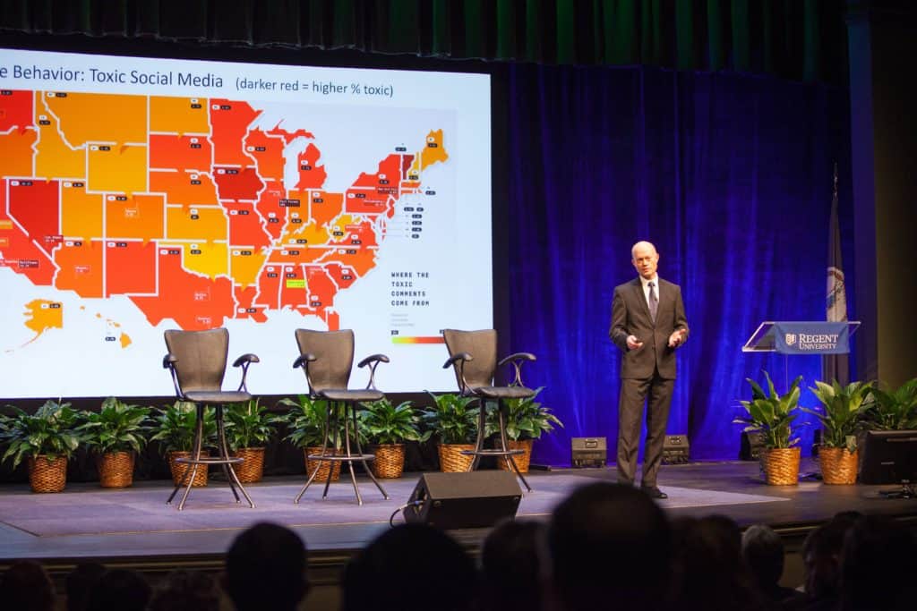 Presenter discusses 'Toxic Social Media' with a U.S. heat map projected behind him showing regional variations in online toxicity.