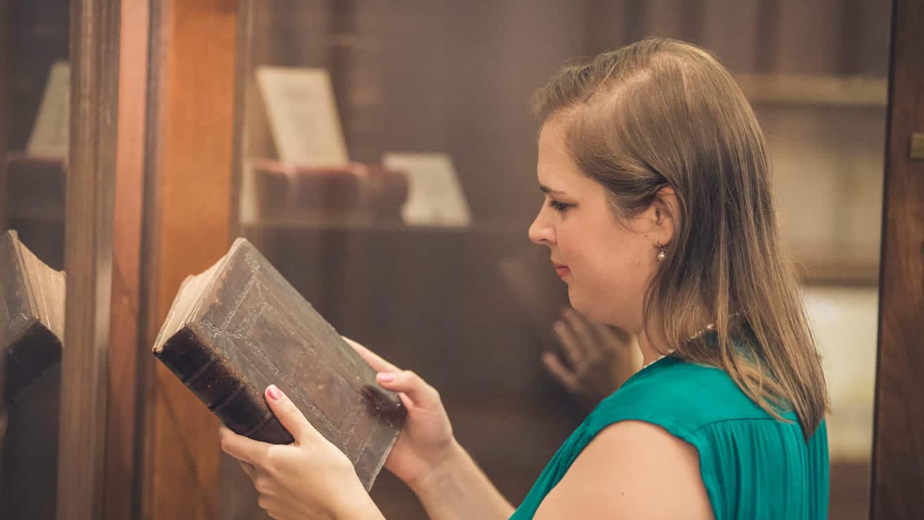 A graduate looks at a book in the library: Explore the Bachelor of Science in Professional Studies - English degree program offered by Regent University.