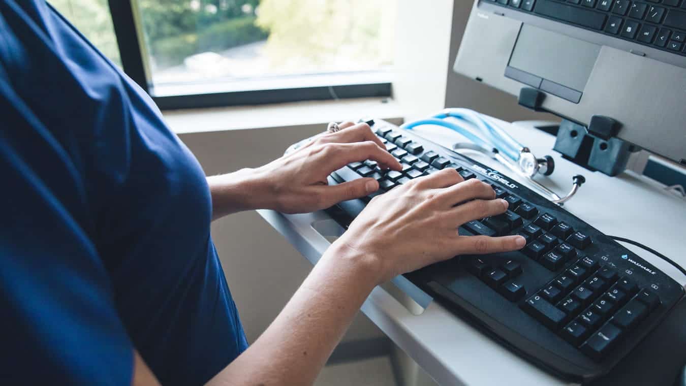A nurse typing on a keyboard: Pursue Regent's B.S. in Professional Studies - Healthcare Management online or in Virginia Beach.