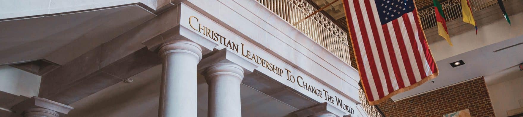 A Regent University student inside a campus building looking out a window and smiling.