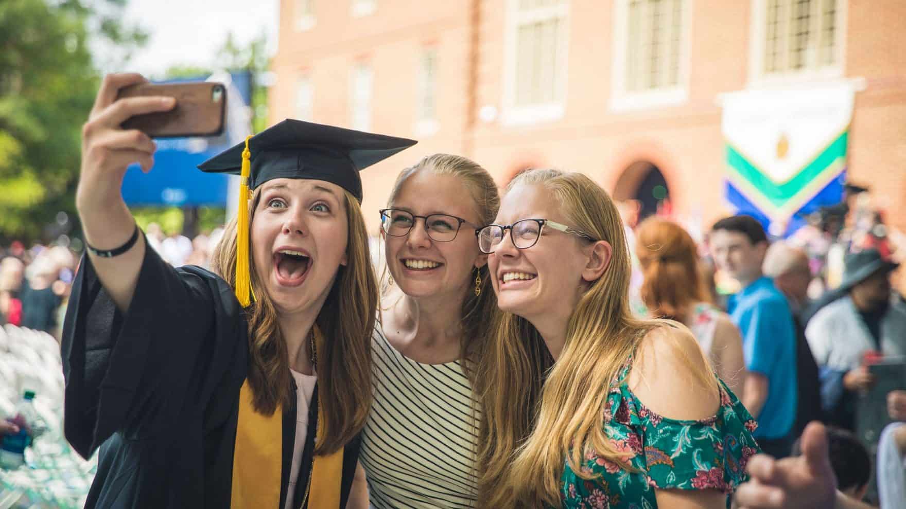 A Regent University graduate takes a selfie with two friends on commencement day in front of the Regent University Library in Virginia Beach.