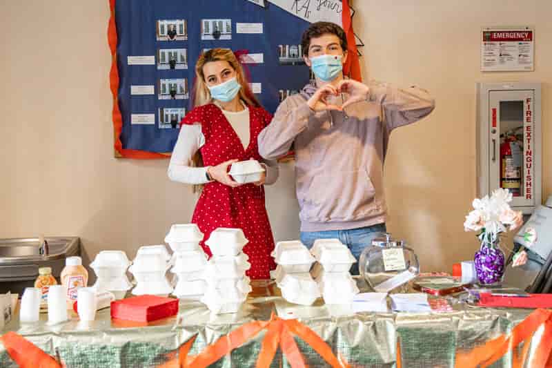 A female student and a male student stand behind a table passing out containers of french fries to students for Spuds With Buds — A Valentine's Day celebration!