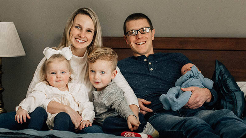 Madison Simons with her husband Joel and three young children, smiling together at home