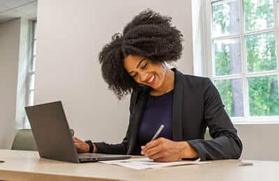 A person writing near her laptop: Prepare for interviews at Regent University's Career Services.