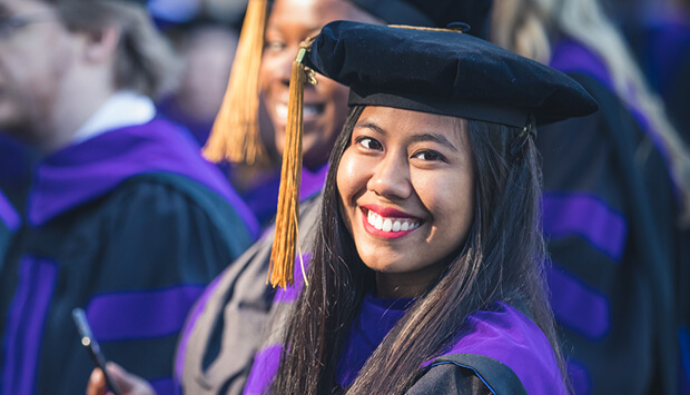 Smiling Regent Law graduate in academic regalia at commencement ceremony.