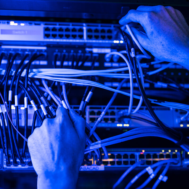 Technician's hands managing network cables and patch panels in a server room illuminated by blue light