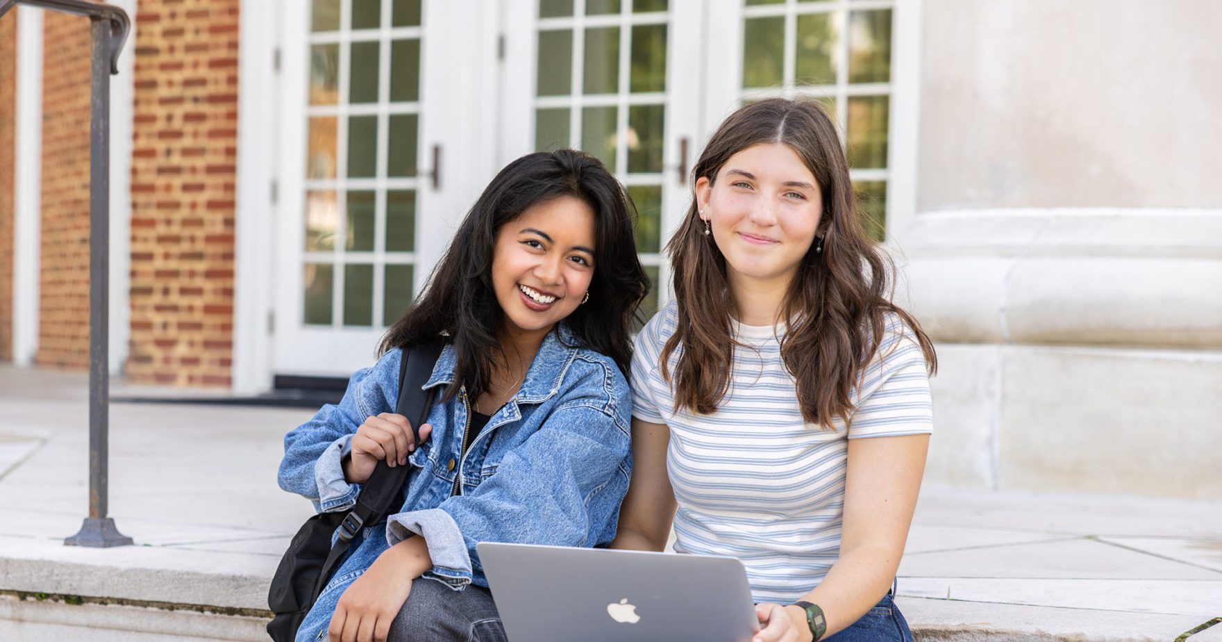 Two Regent University students laughing and doing homework on the steps of the Communication Building at Regent University in Virginia Beach, Virginia.