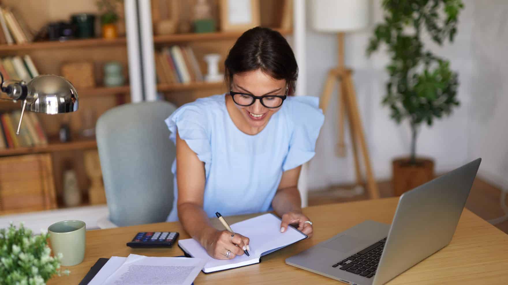 Communications professional working at a desk with a notebook and laptop.