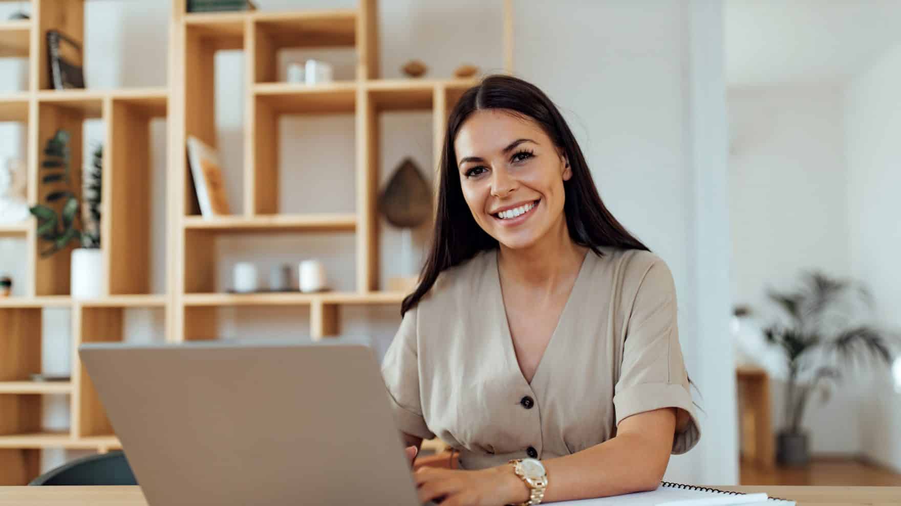 Communications professional smiling and working on a laptop.