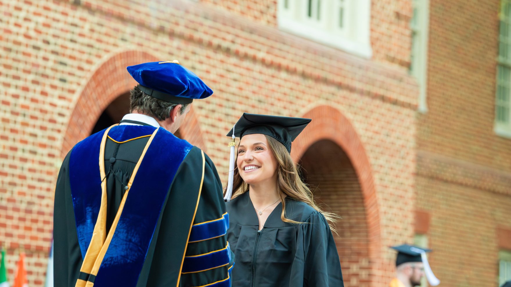 Regent University graduate walking across the stage of the Library Plaza and shaking hands with professor while smiling.