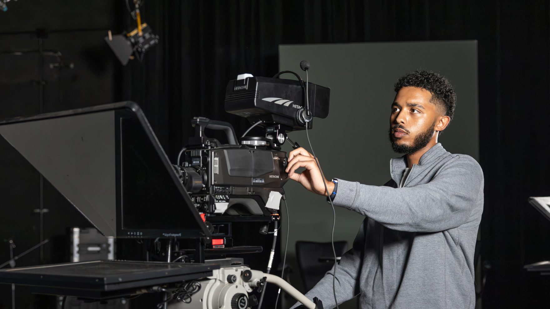 Regent University film student handling a large camera on a set.