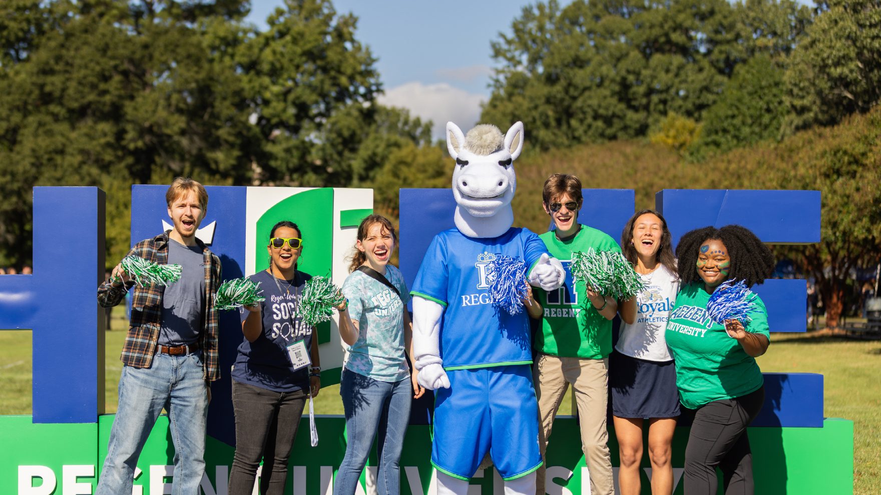 Regent University students standing and smiling with university mascot, Rex the Royal.