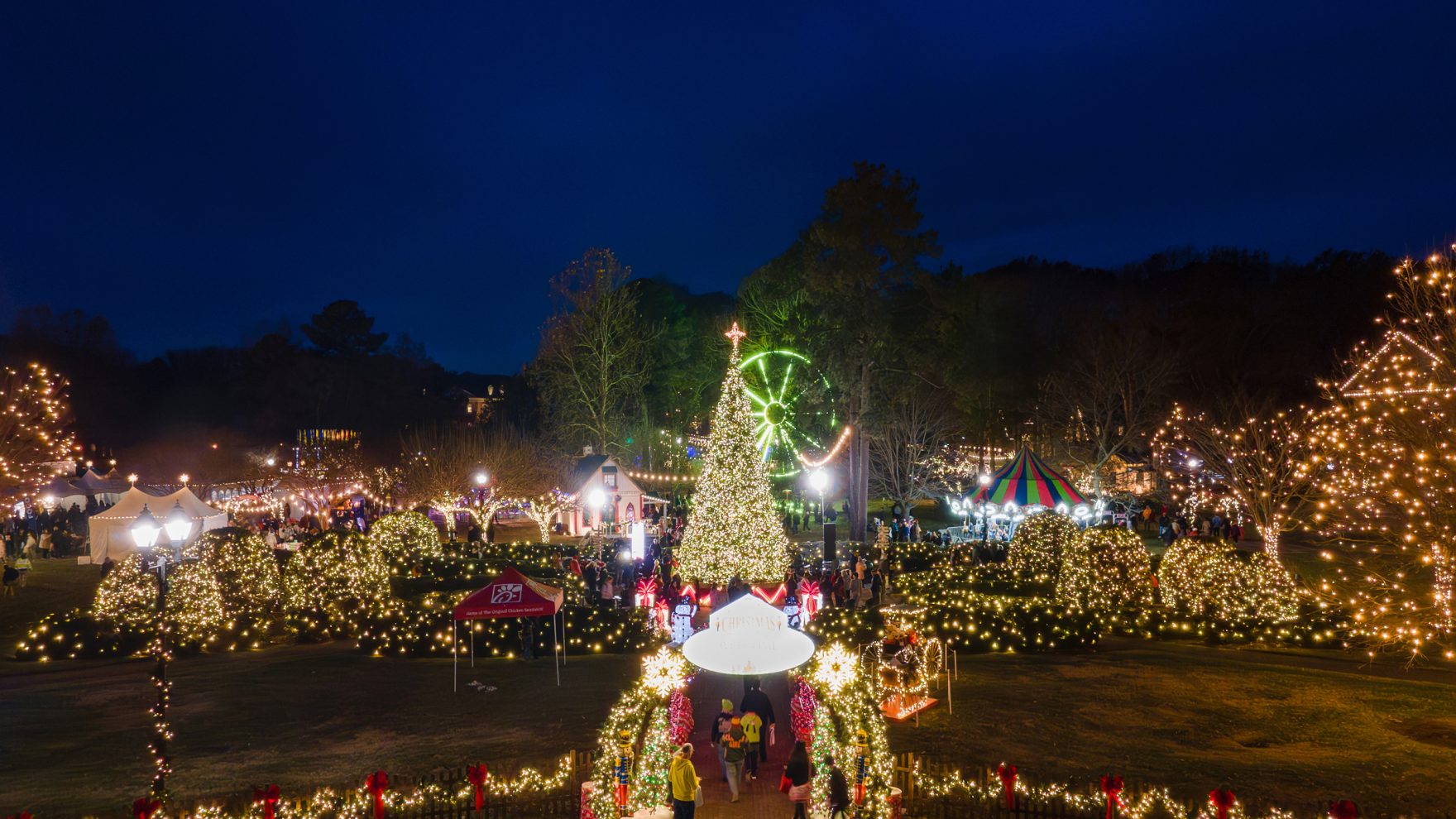 Regent University campus decorated with lights and festivities during Christmas Village event, with the 40-foot Christmas tree lit up at the center of the campus grounds.