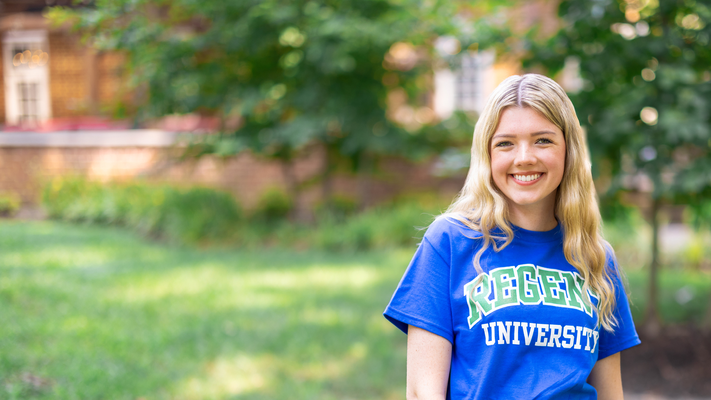 A smiling young woman with long blonde hair wears a blue
